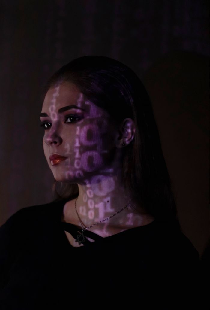 Artistic portrait of a woman with binary code projected on her face in a dark room.