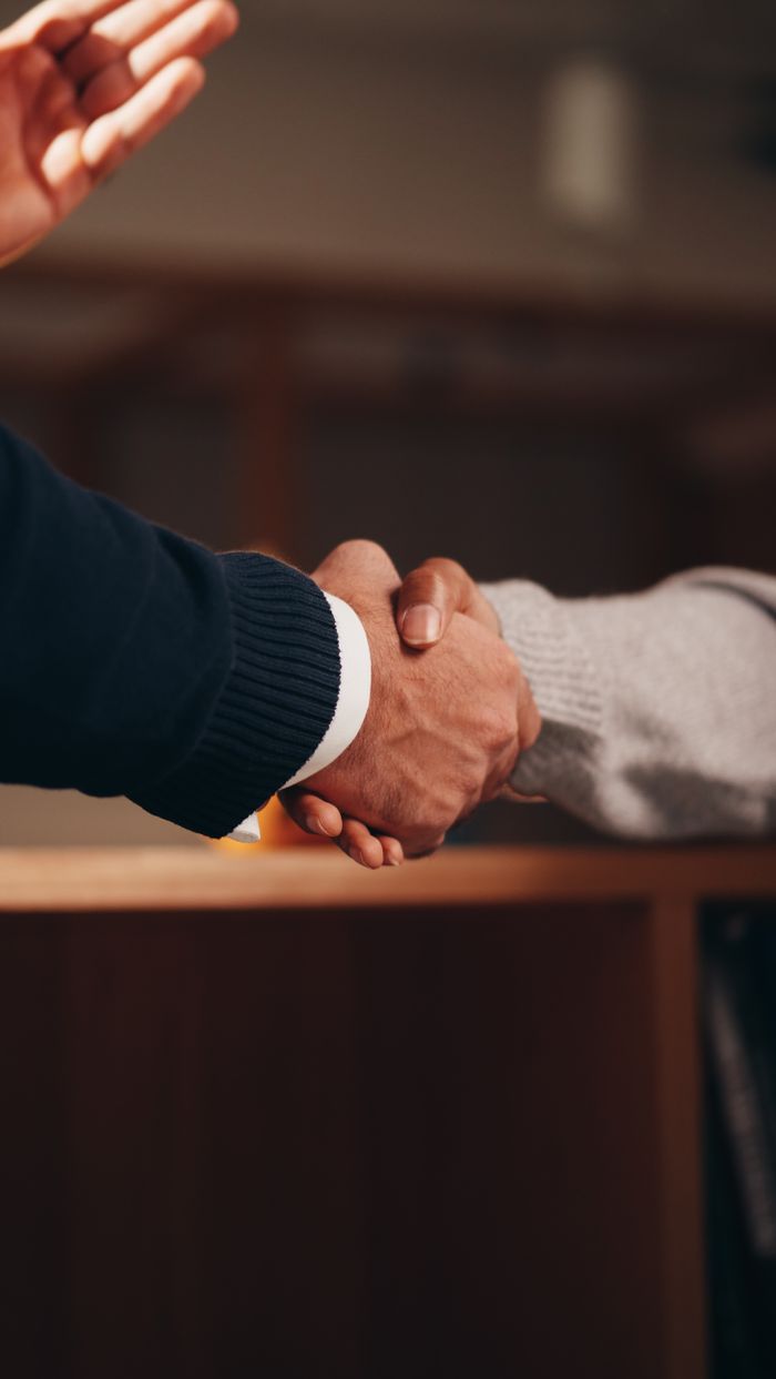 contact-bg Two hands shaking in a professional setting, symbolizing business deal or agreement.